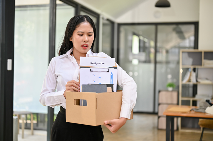 An unemployed Asian female office worker holding a cardboard box with her belongings. gran-tierra-energy-layoffs-know-your-rights