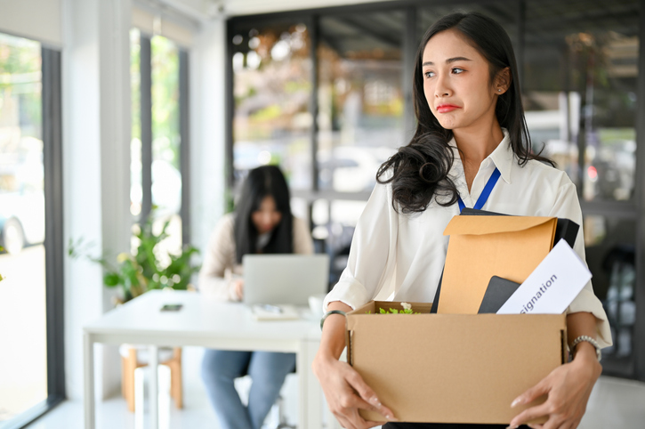 Crying Asian female office worker holding a cardboard box with her stuff, being fired from her boss hive-blockchain-technologies-layoffs-know-your-rights