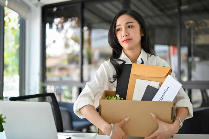 Unhappy Asian female office worker carrying her belongings and a resignation letter. job failure western-copper-and-gold-layoffs-know-your-rights